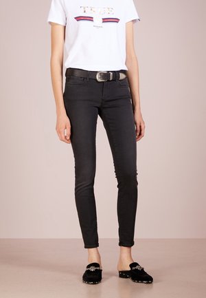 Jeans negros ajustados con un corte de cintura media, que cuentan con cinco bolsillos y un cinturón de cuero. Combinados con una camiseta gráfica blanca y zapatos negros tipo slip-on.