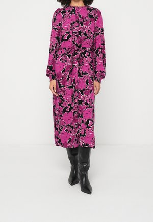 Femme portant une robe à manches longues, mi-longue, à imprimé floral rose et noir, associée à des bottes noires pointues montantes jusqu'aux genoux.