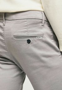 Grå bomuldsbukser med en baglomme med knaplukning og et lille mærketikette. Glat tekstur og skræddersyet pasform.