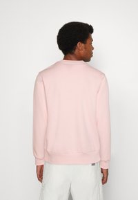 Sweatshirt rose clair fabriqué en tissu doux, avec un col rond, des poignets et un ourlet côtelés, un ajustement décontracté et un design minimaliste.