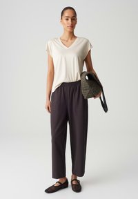 Beige V-hals t-shirt, zwarte elastische broek met zakken, zwarte geweven tas en zwarte mesh sandalen. Eenvoudige, casual outfit.
