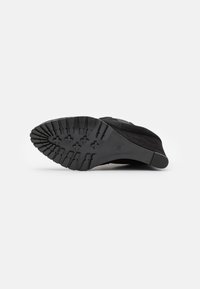 Semelle de chaussure en suede noir avec un motif en caoutchouc texturé, présentant une forme arrondie, un talon plat, et l'indication de taille '38' imprimée dessus.
