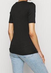 Camiseta negra de manga corta con escote redondeado, diseño ajustado y textura de tela suave, combinada con jeans de color azul claro.