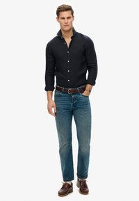 Mannen donkerblauwe button-up shirt met lange mouwen, gecombineerd met lichtblauwe jeans en bruine veterschoenen. Opvallende details zijn onder andere een kraag.