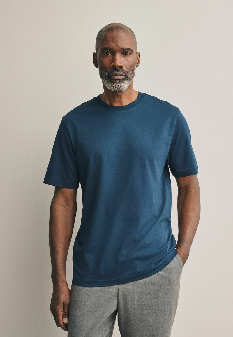 Camiseta de algodón azul marino con cuello redondo y mangas cortas, con una textura suave, combinada con pantalones gris claro.