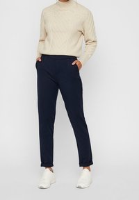 Beżowy sweter z włókna kablowego z golfem oraz granatowe spodnie o tapered fit z bocznymi kieszeniami, zestawione z białymi trampkami, z podwiniętymi mankietami.