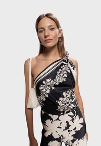 Haut asymétrique à une épaule avec un imprimé floral noir et blanc, une texture satinée et un nœud décoratif à l'épaule ; assorti à un pantalon à motifs.