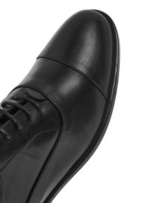 Chaussure habillée en cuir noir avec une finition lisse, un bout rond, un design à lacets et de subtils détails de couture sur le dessus.