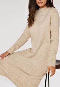Robe en tricot beige avec un col montant et des manches longues. Présente des accents côtelés aux poignets et à l'ourlet, avec une coupe décontractée.