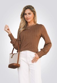 Bruine geribde lange mouwen top met knopenaccenten bij de manchetten, gecombineerd met witte high-waisted broek en een handtas in tan en crème.