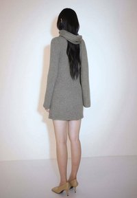 Robe en maille vert pâle avec un col roulé, une texture côtelée, des manches longues et une silhouette ajustée, associée à des talons beiges.