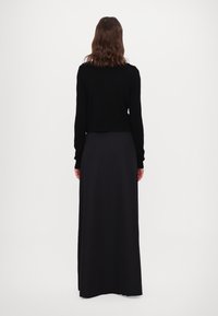 Maglione cropped nero con maniche lunghe abbinato a una gonna maxi nera aderente, dalla texture liscia e senza motivi o accenti visibili.