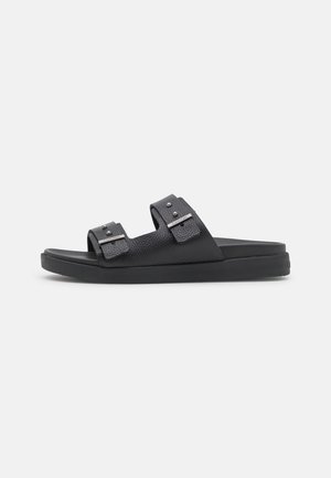 Black sandals with two adjustable straps, textured material, silver hardware accents, and a cushioned black sole.