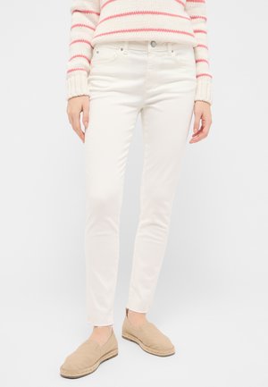 Weiße, schmale Jeans mit glatter Textur, Fünf-Taschen-Design und fransigen Säumen, kombiniert mit hellbeigen Slippern.