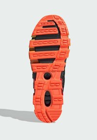 Crna atletska cipela s gumenim potplatom debljine s teksturiranim narančastim slojem, koji ima utore i rezove za prianjanje i fleksibilnost.