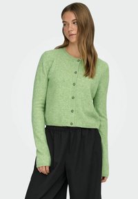 Heleroheline lühendatud kardigan pehmest kangast, millel on ümar kaelus, n�ööpidega esitasku ja soonikkoes varrukasuunad, kombineeritud mustade laia säärega pükstega.