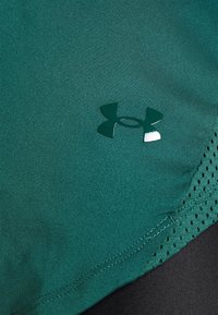 Zielona sportowa koszulka wykonana z gładkiej tkaniny, z trójkątnym logo i teksturowanymi siateczkowymi akcentami. Szwy są starannie wykończone.