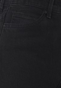 Jeans de mezclilla negra con una vista en primer plano de la tela texturizada, costuras sutiles y un bolsillo delantero con un borde redondeado.