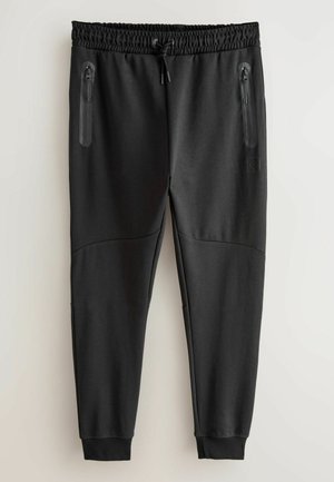 Fekete melegítőnadrág elasztikus derékkal, állítható zsinórral és két cipzáras zsebbel. Simább anyag, tapered lábakkal és bordás mandzsettákkal.