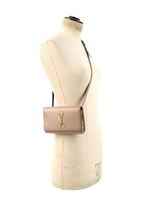 Sac bandoulière en cuir beige avec un logo YSL doré présenté sur un mannequin de couture couleur crème.
