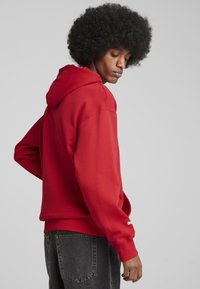 Rød hættetrøje med snøre i hætten, ribbede manchetter og kant. Blødt stof med en struktureret overflade. Sammen med mørke jeans. Enkel logo-detalje.