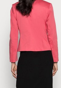 Koralfarvet skræddersyet blazer med lange ærmer, glat stof, tætsiddende form og lige kant, parret med en sort ribbet nederdel.
