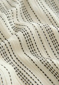Tissu textile avec un fond léger et crémeux, orné de fines lignes horizontales noires espacées régulièrement et d'accents en pointillé tout au long.