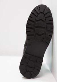 Suela de bota de goma negra con un patrón de relieve robusto, que presenta surcos profundos y tracción incorporada para un uso duradero y antideslizante.