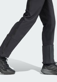 Pantalons d'extérieur noirs avec poches zippées, design fuselé et tissu texturé, associés à des chaussures de randonnée noires avec une semelle robuste.