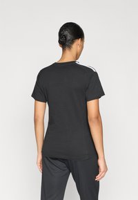 Μαύρο βαμβακερό t-shirt με κοντά μανίκια, που διαθέτει λευκές ρίγες κατά μήκος των ραφών των ώμων, στρογγυλή λαιμόκοψη και άνετη εφαρμογή.