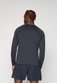 Langärmliges, dunkelblaues Funktionsshirt mit Raglanärmeln und glatter Textur, kombiniert mit passenden Shorts. Minimalistisches Design.
