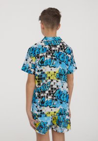 Camicia a maniche corte con colletto, caratterizzata da una stampa di graffiti colorata nei toni del blu, giallo e nero. Il materiale sembra leggero e casual.