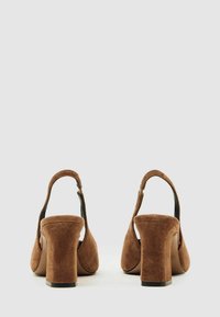 Smeđu zlatnu visokih potpetica od zamska s otvorenom petom i debelim blok petama. Cipele imaju glatku završnu obradu i zakrivljen oblik pete.