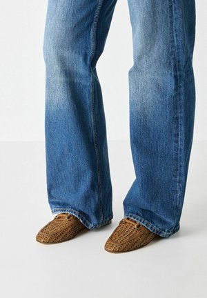 Brown woven leather shoes with a pointed toe, paired with light blue flared jeans, featuring a faded texture and visible stitching details.