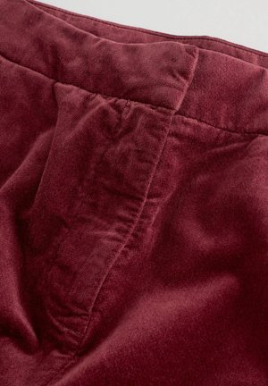 Burgundská, měkká tkanina s hladkým povrchem; obsahuje pás a detaily švů, což ukazuje na neformální design.