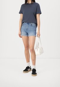 Marine crewneck t-shirt, lichtblauwe denim shorts met opgerolde mouwen, zwarte sneakers met witte strepen en een kleine witte handtas.