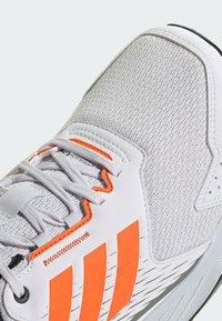 Lichtgrijze sportschoen met oranje accenten, gestructureerde bovenkant en witte veters. Bevat drie gedurfde oranje strepen en een slank ontwerp.