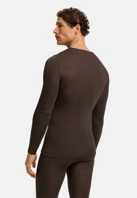 Camiseta térmica de manga larga marrón con cuello redondo, diseño ajustado y puños acanalados. El material parece suave y liviano para mayor comodidad.