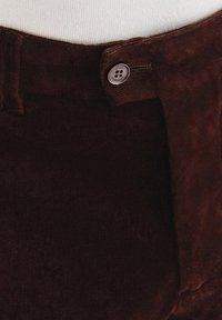 Brązowe spodnie kordowe o gładkiej teksturze, z zapięciem na guzik i zamek błyskawiczny, oraz talią z szlufkami na pasek.