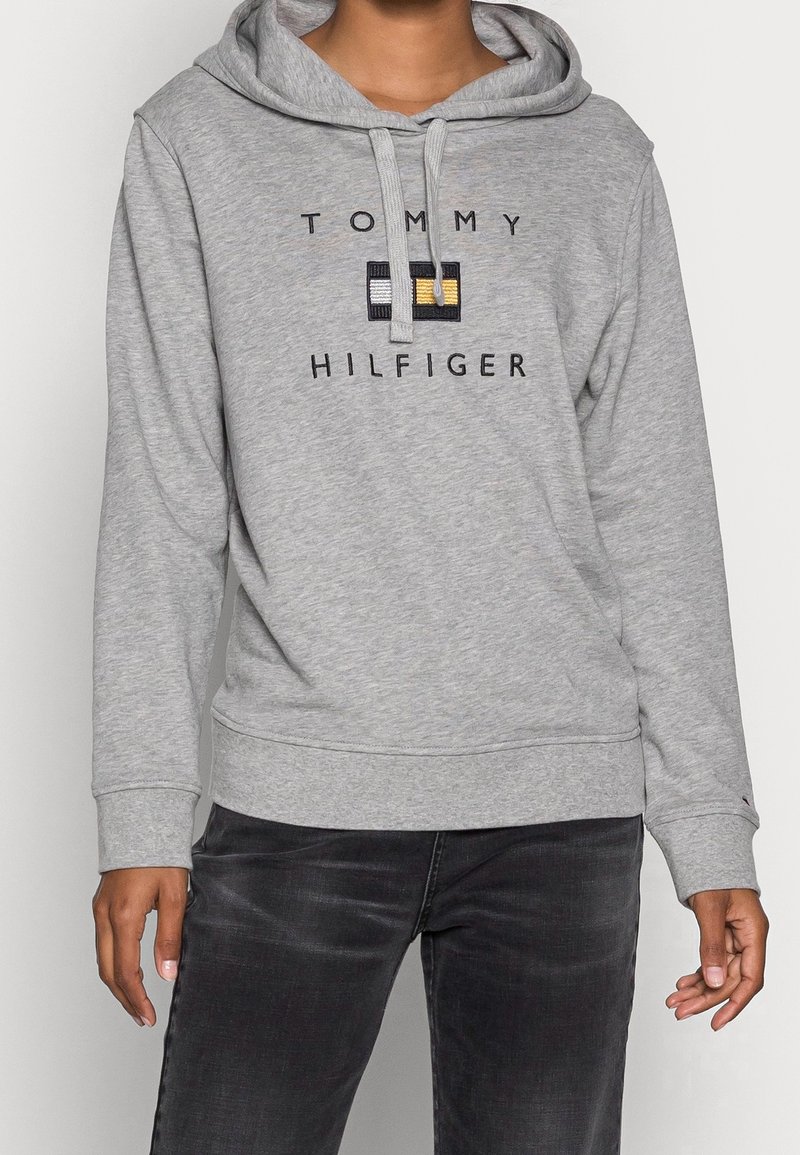Felpa grigia con cappuccio, tasca a marsupio, cappuccio con cordino e logo "TOMMY HILFIGER" in rilievo con accenti a blocchi di colore sul petto.