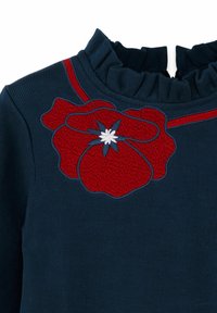 Marineblaue Rippenstoffbluse mit einem Rüschenausschnitt und roter Blumenstickerei sowie einem weißen und blauen Blumenakzent in der Nähe des Ausschnitts.