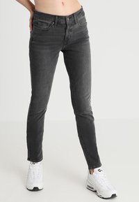 Svarta slim-fit jeans med en urtvättad textur, med klassisk femfickedesign och knäppning framtill. I kombination med vita sportskor.