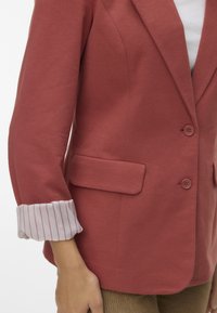 Blazer u boji hrđe s prilagođenim dizajnom, dva gumba i džepom s krpom. Manžeta s lakom prugastom tkaninom. Teksturirani materijal.