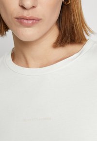 Weißes Baumwoll-T-Shirt mit rundem Ausschnitt, das dezenten "Marc O'Polo DENIM" Schriftzug in hellem Beige und weicher Textur aufweist.