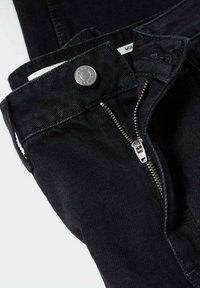 Jean en denim noir avec un bouton métallique, une fermeture éclair et des détails cousus. Possède un design classique et une finition douce et texturée.