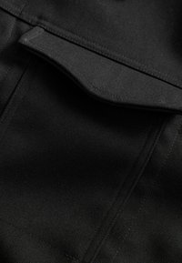 Sort stof med en glat tekstur og subtil glans. Har en foldet lommeflap og rene syninger, der fremviser moderne designelementer.