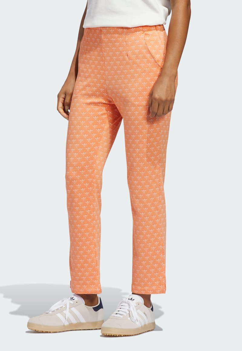 Παντελόνια πορτοκαλί με σχέδιο λουλουδιών, με πλαϊνές τσέπες και εφαρμοστή γραμμή, συνδυασμένα με μπεζ και ναυτικά αθλητικά παπούτσια.