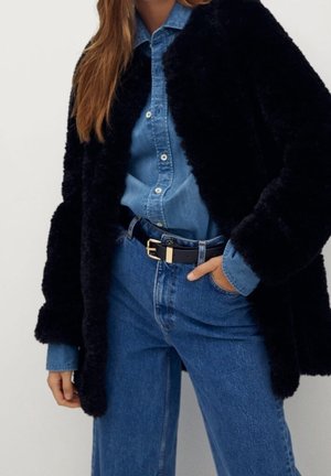 Cappotto esterno nero e soffice, camicia di jeans, jeans blu a vita alta, cintura nera con hardware dorato, texture liscia, look casual a strati.
