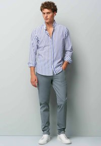 Blue and white striped button-up shirt, paired with gray trousers and white sneakers. The shirt features long sleeves and a slightly open collar.