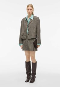 Bruine tweed blazer met twee zakken, gecombineerd met een lichtblauwe blouse en een bijpassende mini rok. Bruine leren knielange laarzen en een clutch.